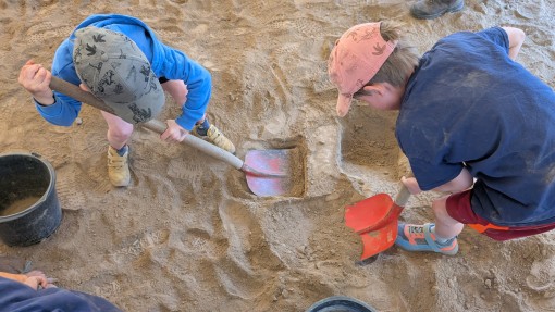 Zwei kleine Jungen mit Kappen schaufeln eifrig im Sand.