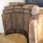 Dargestellt wird ein römischer Steinbrunnen, dessen Steine hochkant einen Viertelkreis andeuten und in Sand eingebettet sind.
