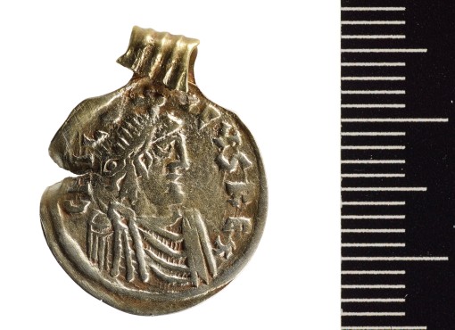 Das Foto zeigt eine Goldmünze mit Öse als Anhänger umgearbeitet. Die Vorderseite zeigt einen männlichen Kopf im Profil, der durch Diadem und Mantel als Herrscher charakterisiert ist. Der Rand ist links verbogen und mit unlesbarer Inschrift versehen. 